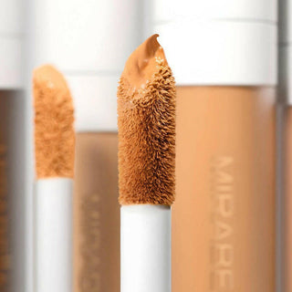 Up close image of Mirabella's Perfecting Concealer doe foot applicator wand with bottles of concealer in the background.