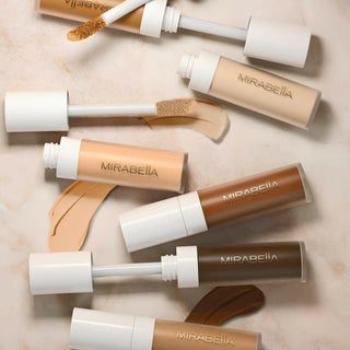 Invincible For All Perfecting Concealer on a marbled tan background showing a diverse shade range of opened concealers with swatches.