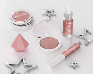 Mirabella Illuminizing Kit, featuring a shimmering powder, glow drops, lip gloss & diamond blender sponge on white background with stars.