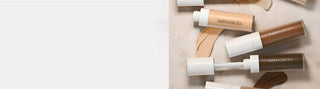 Web banner of diverse swatches & open sleek tube of Mirabella Invincible For Perfecting Concealer: buildable coverage for all with doe-foot.